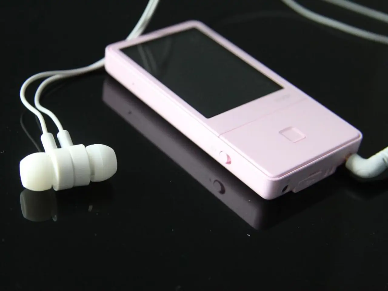 In this picture we can see a pink iPod with white earphones kept on a black surface.