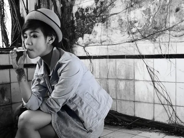 This is the picture of a person wearing jacket and holding the cigarette and sitting on the floor...