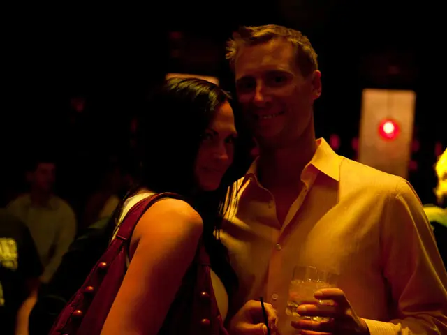 In this image we can see people standing on the floor and one of them is holding a glass tumbler in...