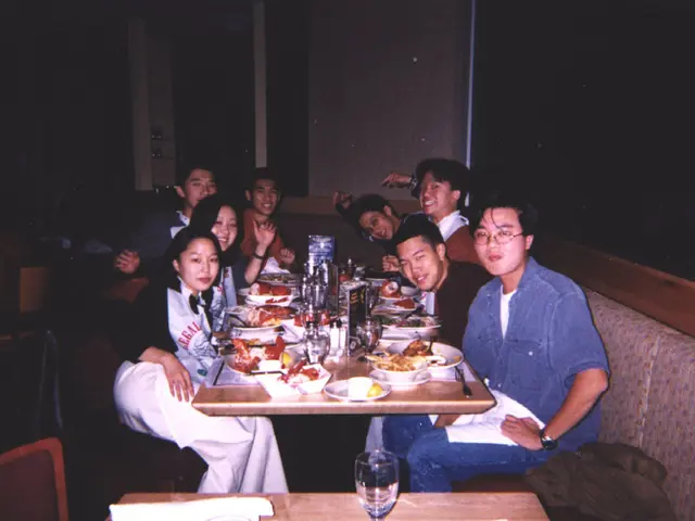 In this picture there are group of people sitting. In between them there is a table with many food...