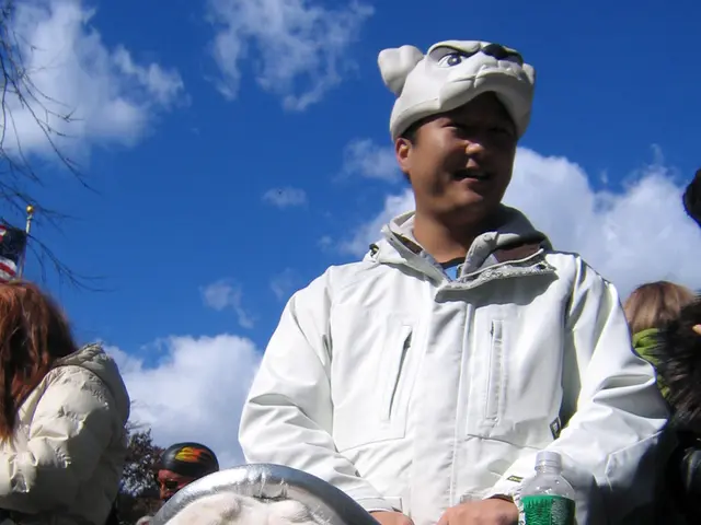 A dog is siting on the stroller. On the stroller there is a bottle and some other items. It is hold...